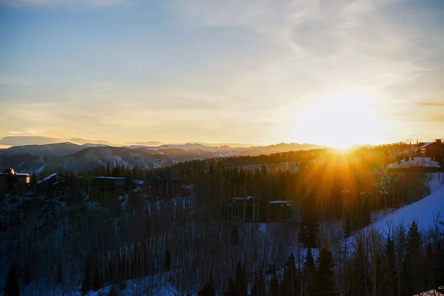 Sunrise over a ski valley, the sun breaking through trees along a ridge.